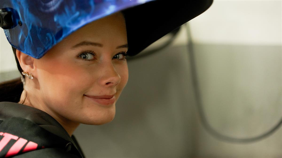 Jente med sveisehatt smiler. Foto - Klikk for stort bilde