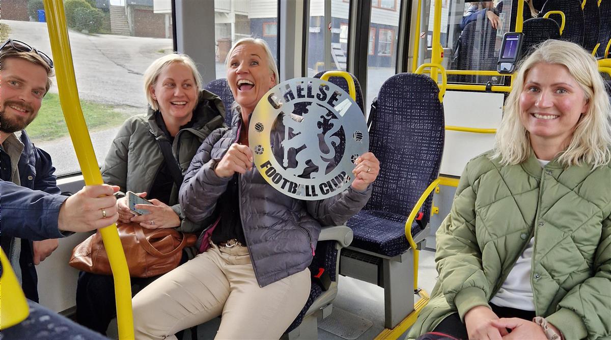 Dame på buss holder et skilt med Chelsea fotballklubbs logo - Klikk for stort bilde