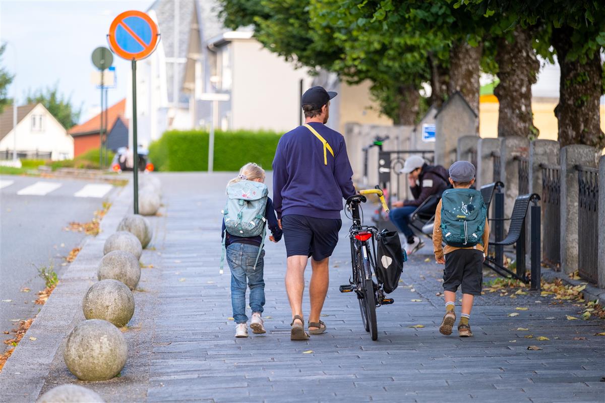 Far med sykkel går sammen med to barn på vei til skolen - Klikk for stort bilde