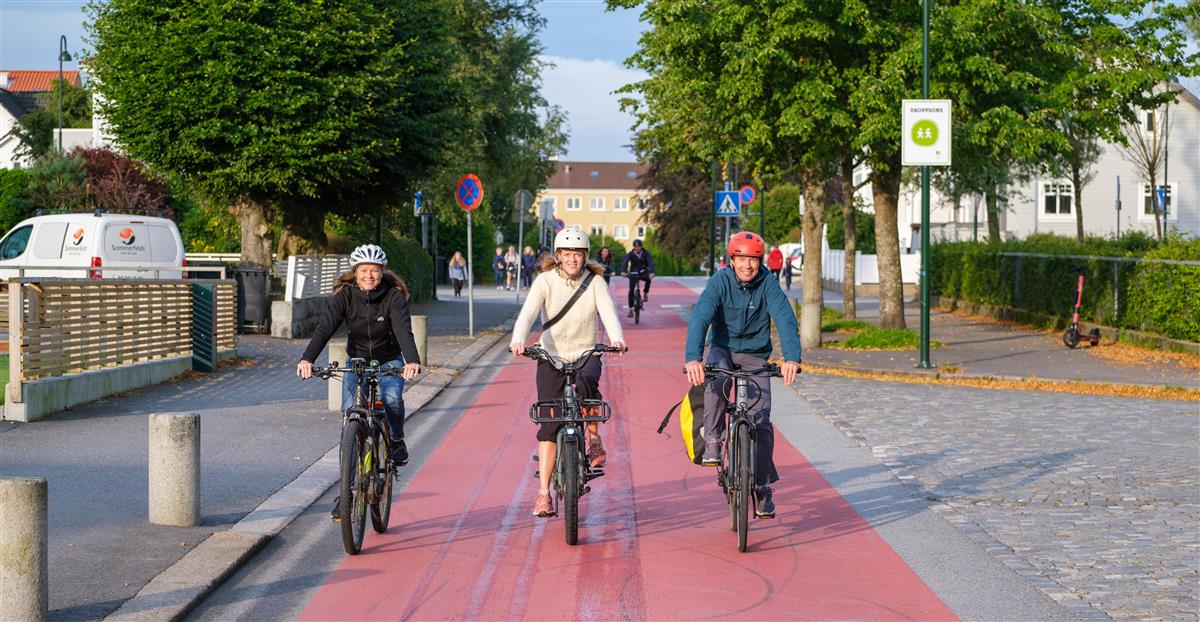 Tre syklister med hjelm sykler mot kamera på rødt dekke. - Klikk for stort bilde